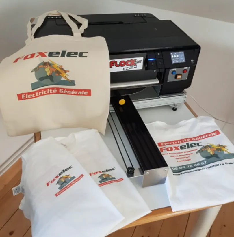 Tote bag et t-shirts imprimés du logo Foxelec, devant l’imprimante DTF de l’atelier